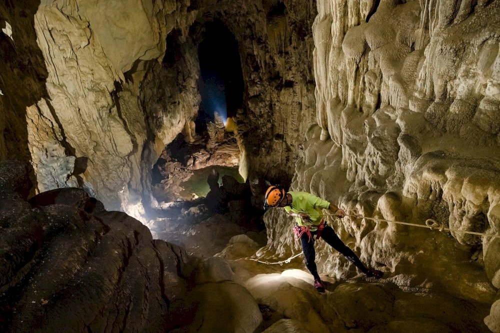 The packing list must include a headlamp, waterproof bags, gloves, and a compact rain jacket for cave conditions 